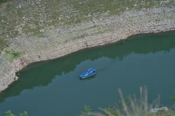 Ein blaues Ausflugsboot fährt durch die Uvac-Schlucht, umgeben von felsigen Ufern und tiefem, grünem Wasser.