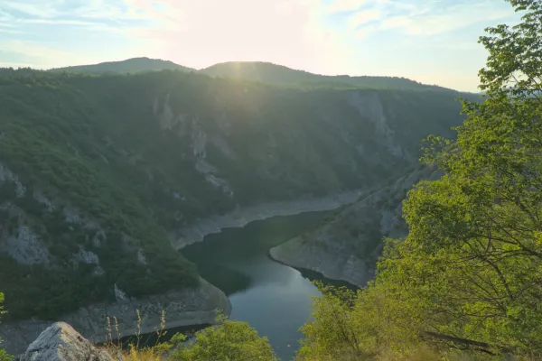 Meander des Uvac-Flusses bei Sonnenuntergang, umgeben von grünen Hügeln und zerklüfteten Klippen.