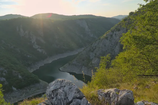 Vista panoramica del Canyon di Uvac in Serbia, con un fiume che serpeggia tra pendii boscosi, illuminato dalla calda luce del tramonto.