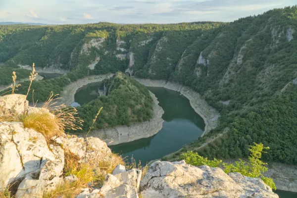Die Uvac-Flussbiegung in Serbien bei Sonnenuntergang mit üppiger Vegetation und felsigen Ufern.