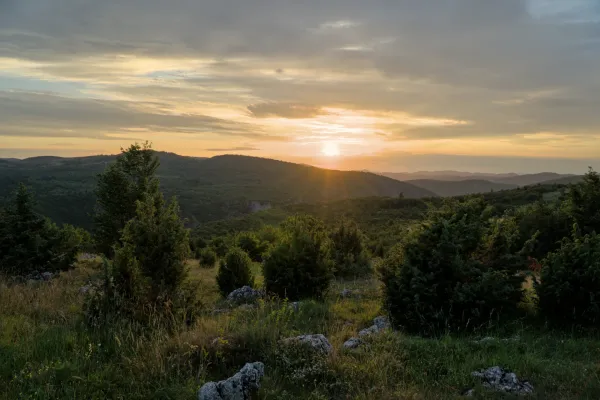Sonnenuntergang über dem Uvac-Tal von Aussichtspunkt Mljetva, Serbien, mit dramatischen Wolken und sonnendurchfluteten Hügeln.