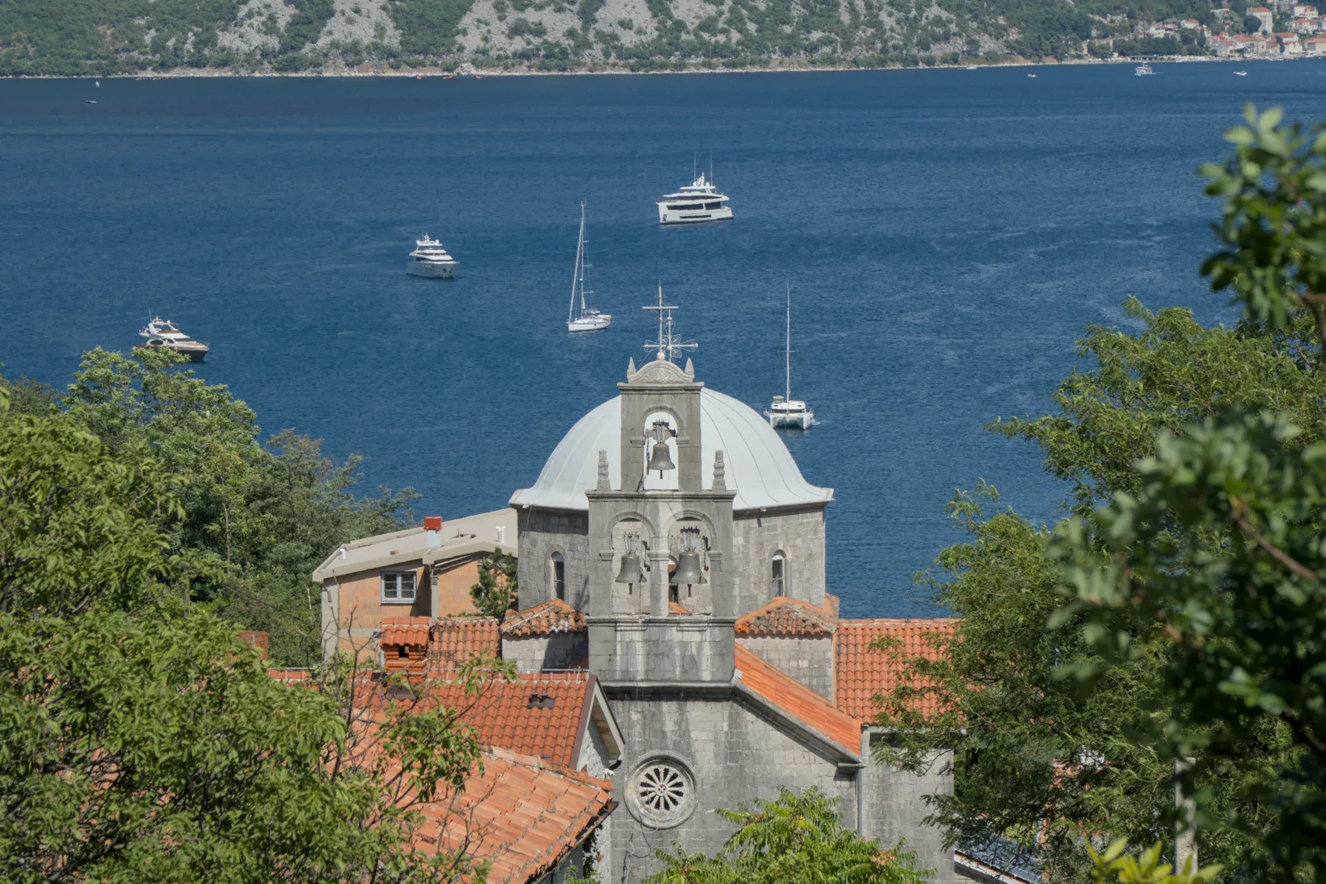 Une église avec un dôme et un clocher se dresse devant la baie de Kotor, Monténégro, près de Morinj, avec des yachts sur l'eau.