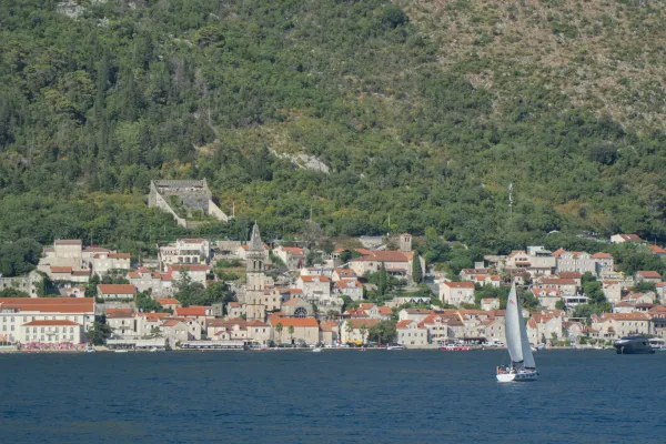 Vista di Perast nella Baia di Kotor con una barca a vela e colline verdi sullo sfondo.