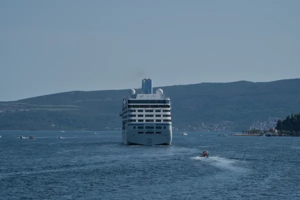 Ein Kreuzfahrtschiff verlässt die Bucht von Kotor, umgeben von blauen Gewässern und grünen Hügeln.