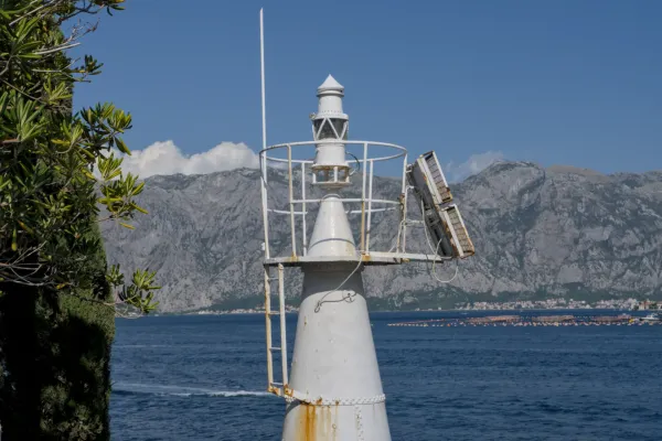 Faro all'ingresso della Baia di Kotor, Montenegro, con il mare turchese e le montagne sullo sfondo.
