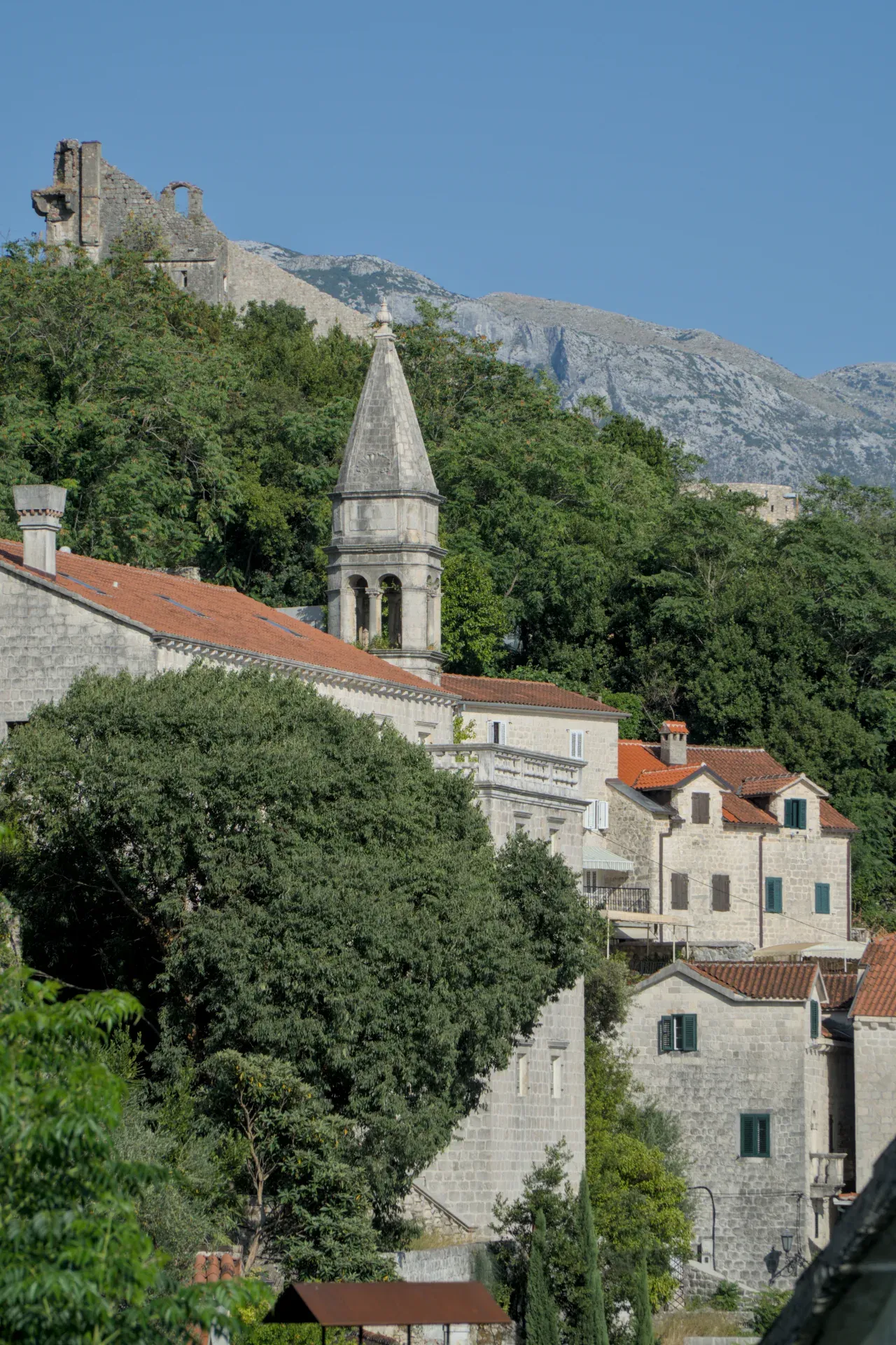 Photographie d'art de Perast, Monténégro, présentant des bâtiments en pierre, un clocher et un arrière-plan montagneux.