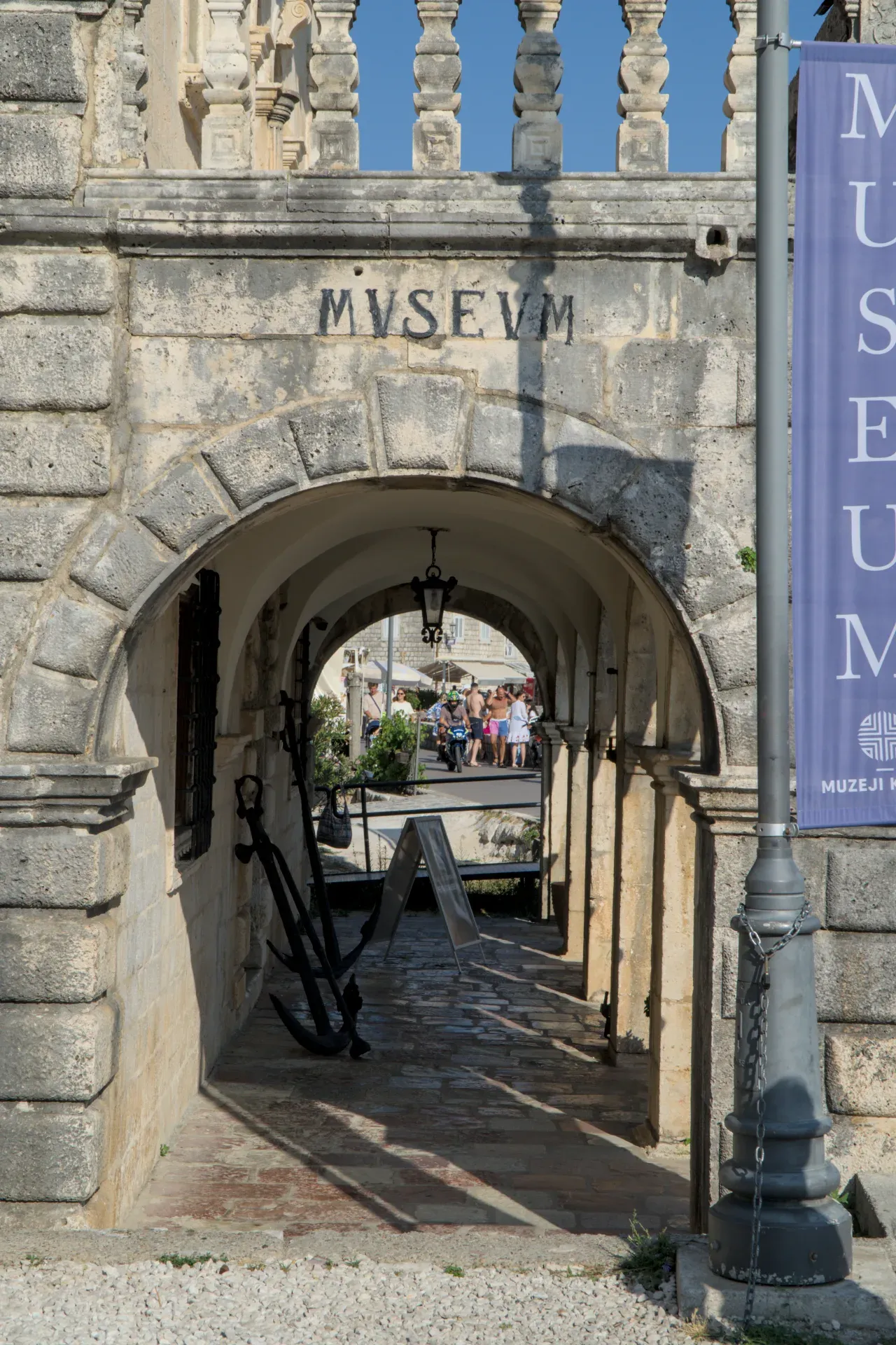 Antiker Torbogen des Museums in Perast, Montenegro, mit historischen Ankern davor und Blick auf belebte Straße.