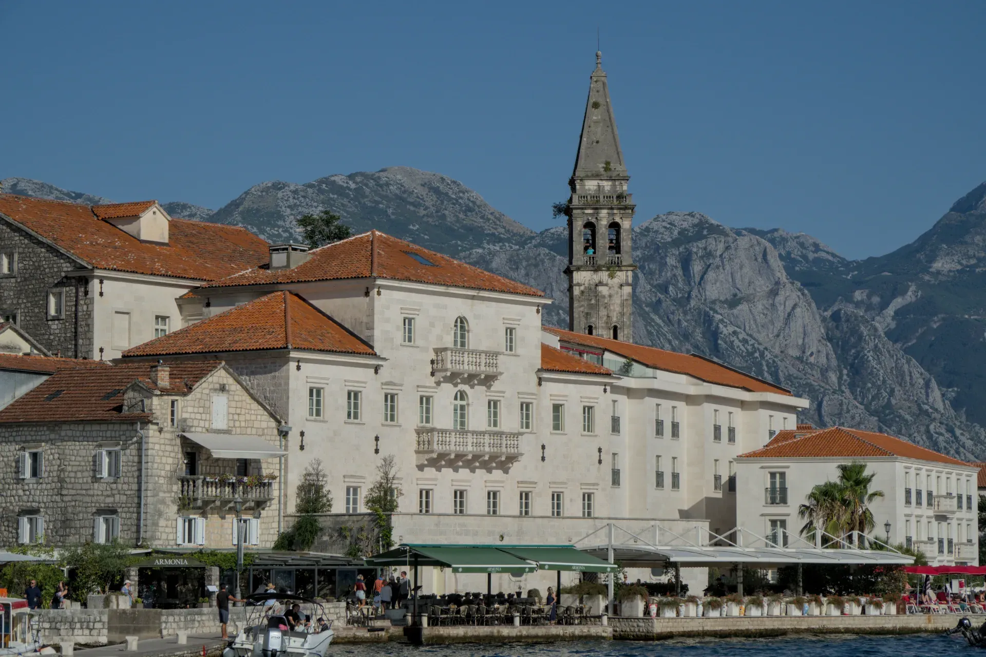 La ville pittoresque de Perast au Monténégro au coucher du soleil, avec ses bâtiments historiques et son clocher sur fond de montagnes.