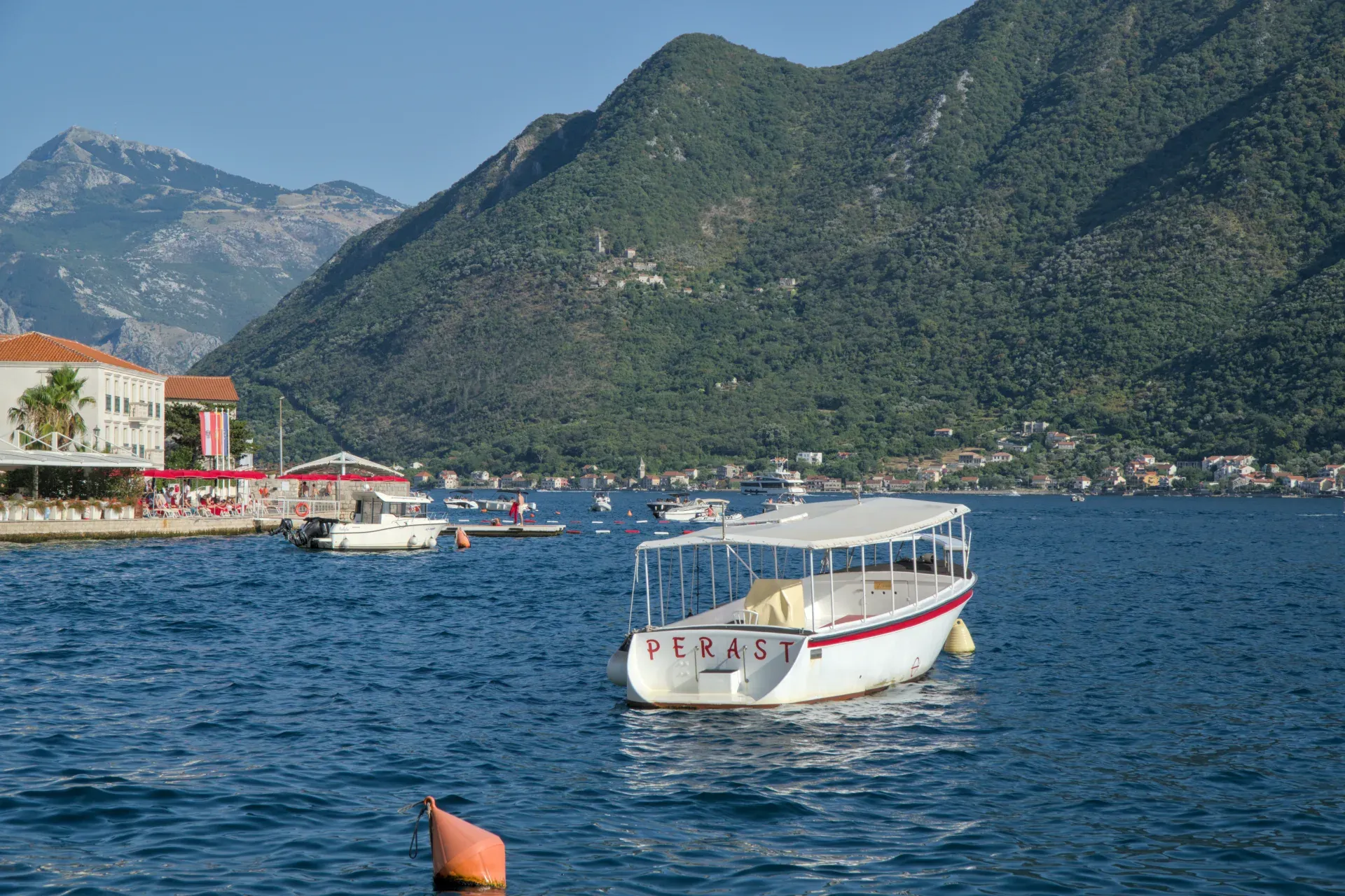 Ein kleines Ausflugsboot mit dem Namen "Perast" ankert ruhig in der Bucht von Kotor, Montenegro, vor der Küste.