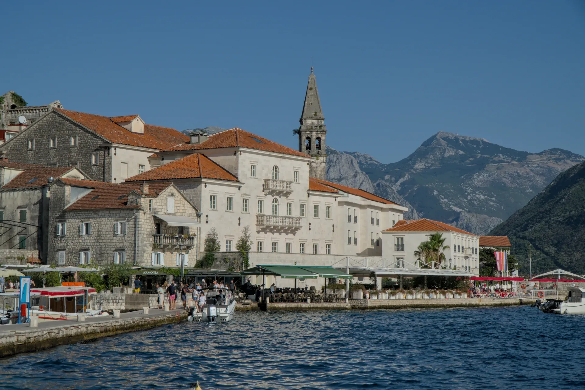 Pogled na Perast u Crnoj Gori pri zalasku sunca sa istorijskim zgradama i planinama u pozadini.