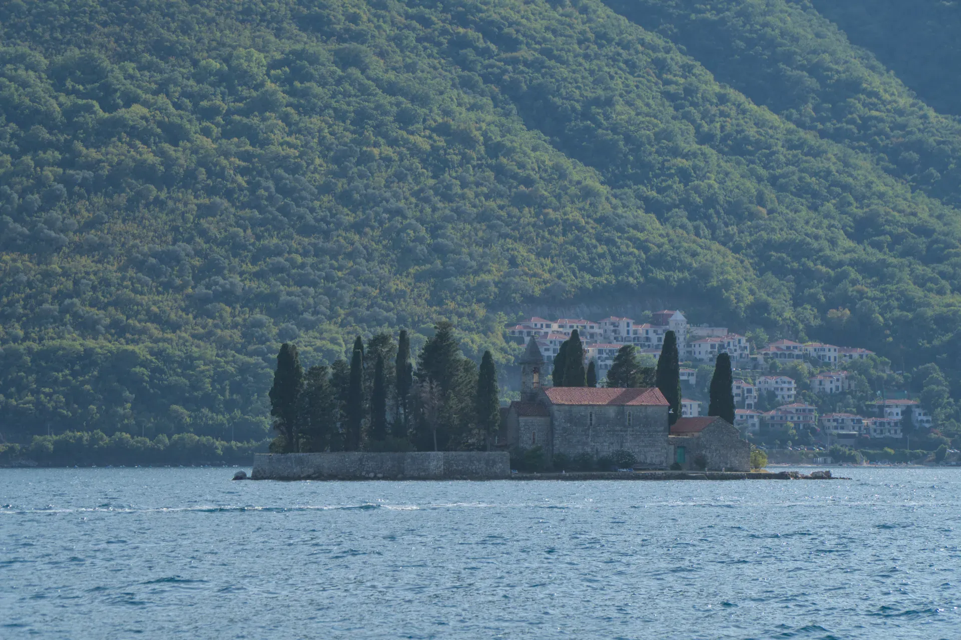 Le monastère Saint-Georges sur une île à Perast, Monténégro, avec une végétation luxuriante en arrière-plan et une eau calme au premier plan.