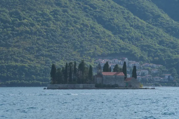 Il Monastero di San Giorgio su un'isola a Perast, Montenegro, con vegetazione lussureggiante sullo sfondo e acqua calma in primo piano.