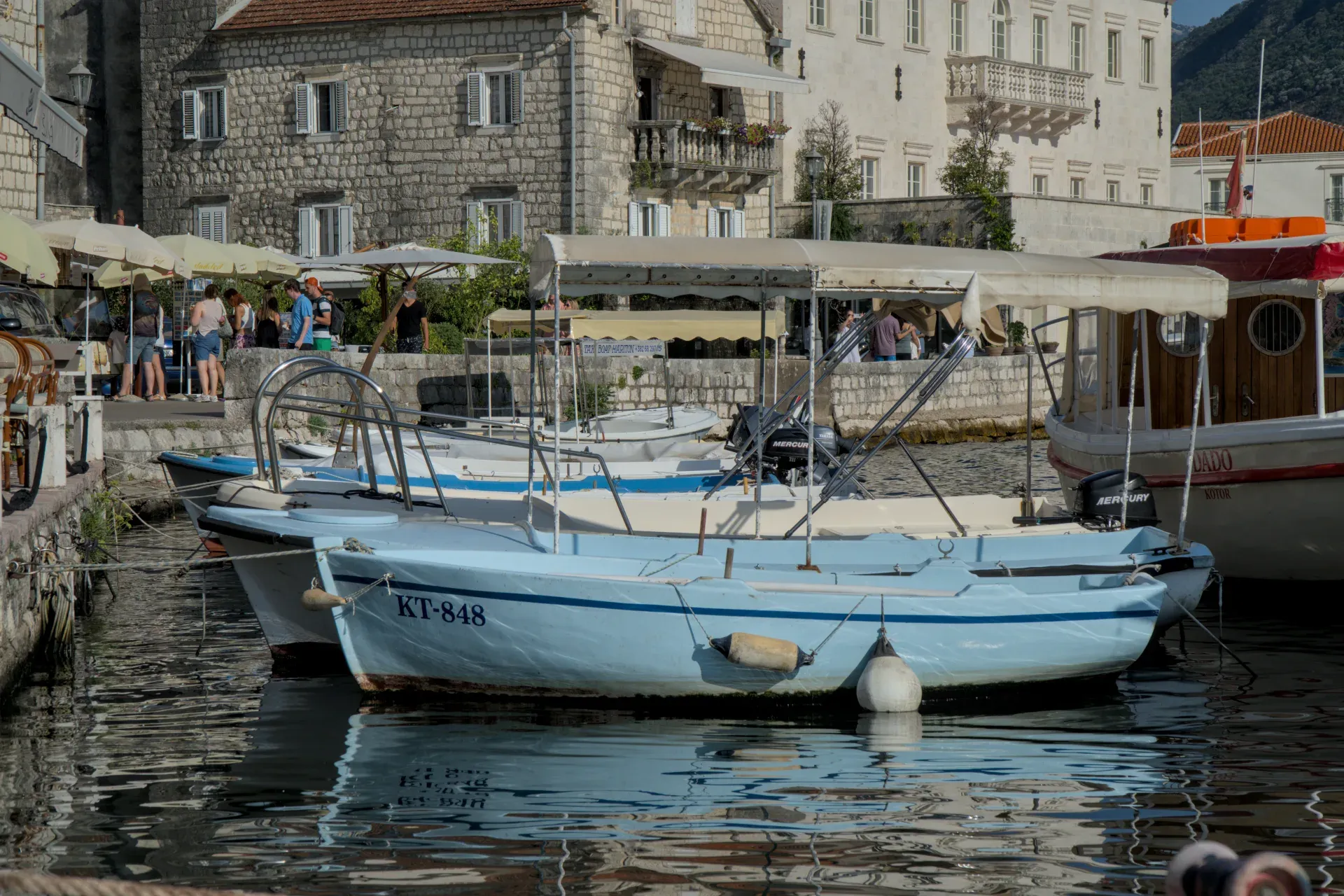 Bilder von Booten im Hafen von Perast, Montenegro, mit Steingebäuden im Hintergrund.