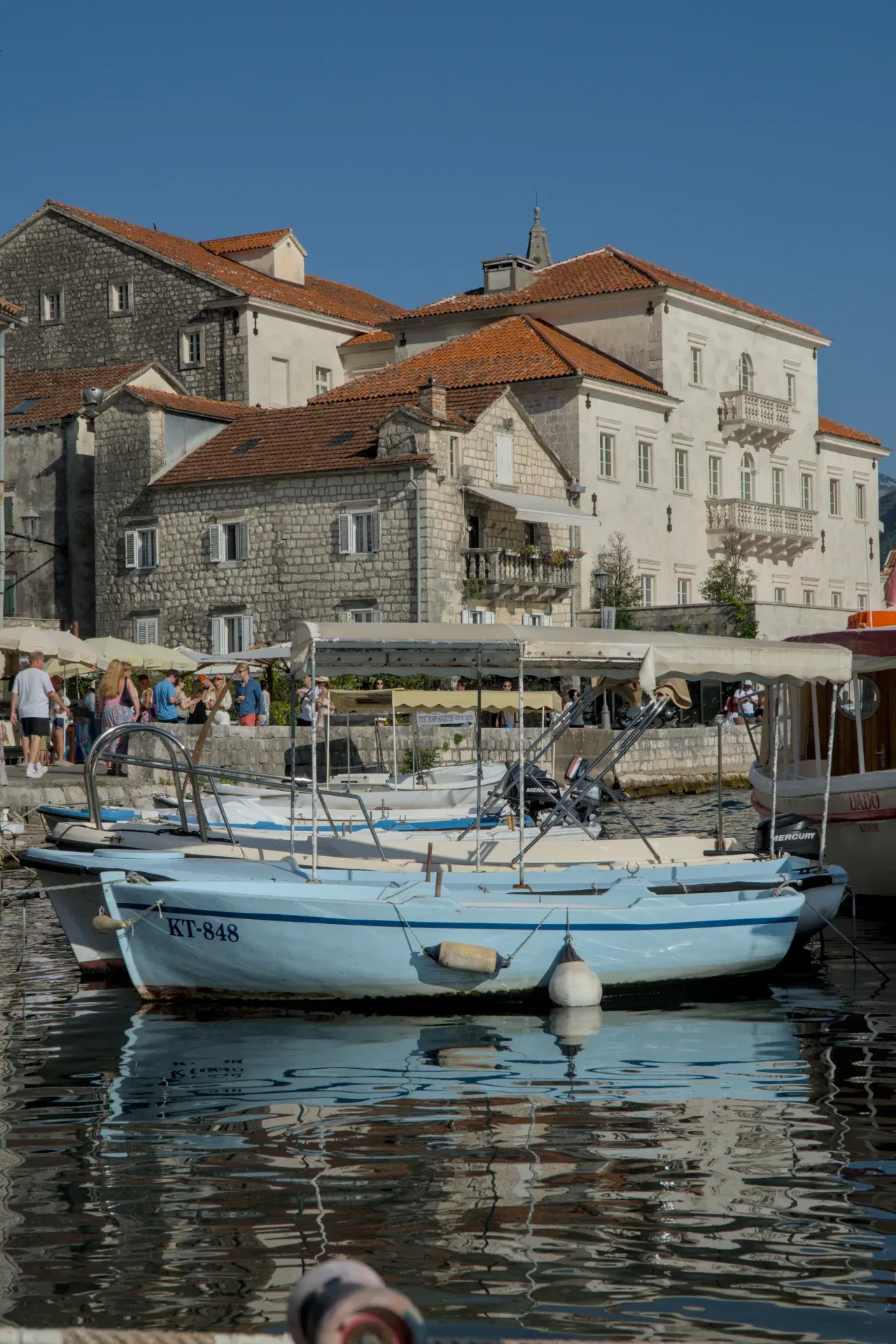 Ein blaues Boot liegt vor Anker in einem malerischen Hafen in Perast, Montenegro, mit historischen Gebäuden im Hintergrund.