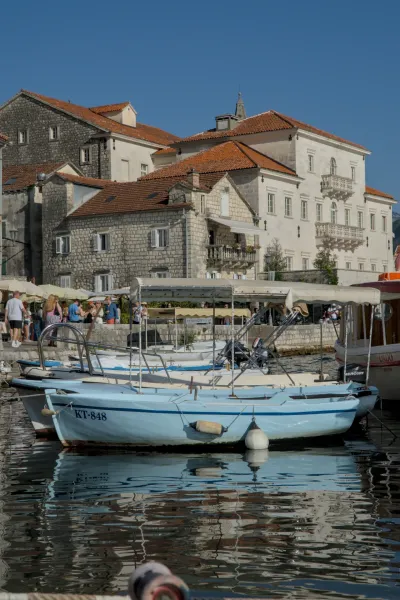 Plavi čamac je usidren u slikovitoj luci Perast, Crna Gora, sa istorijskim zgradama u pozadini.