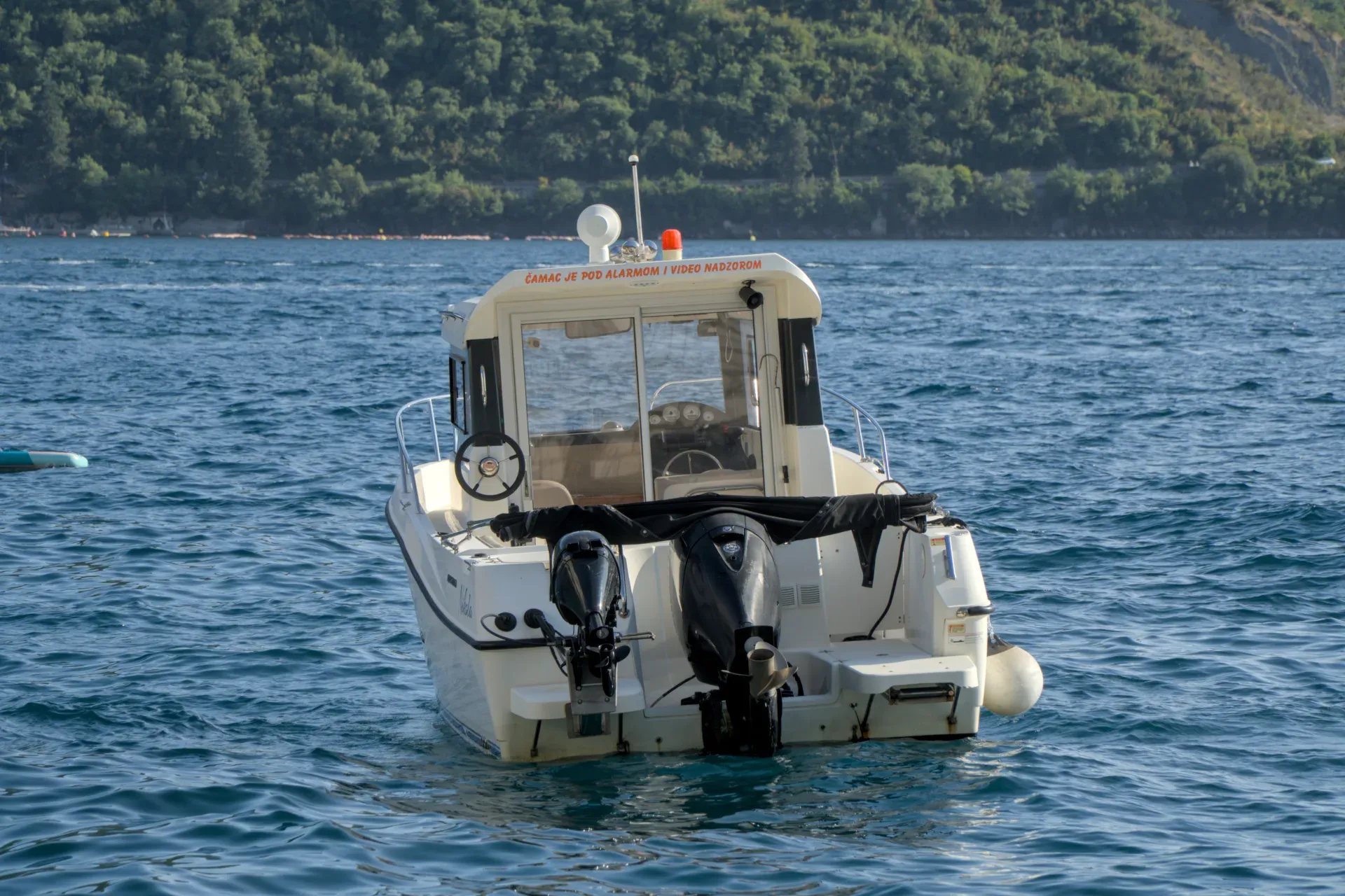 Čamac čeka turiste u mirnim vodama Perasta, Crna Gora, sa zelenim brdima u pozadini.