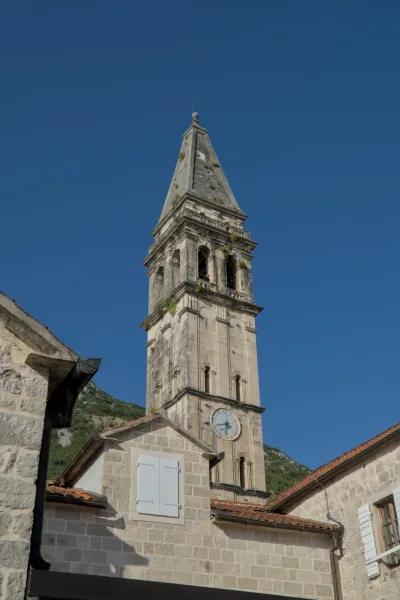 Il famoso campanile di Perasto, Montenegro, sotto un cielo blu brillante, con edifici in pietra in primo piano.