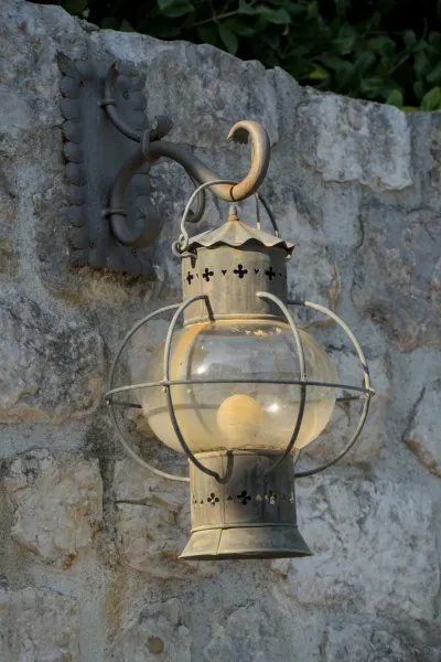 Une lanterne ancienne et ronde en métal et verre est suspendue à un mur de pierre à Perast.