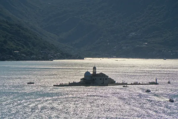 Blick auf die Insel Gospa od Škrpelja bei Sonnenuntergang, mit schattigen Bergen im Hintergrund und glitzerndem Wasser, aufgenommen vom Turm in Perast.