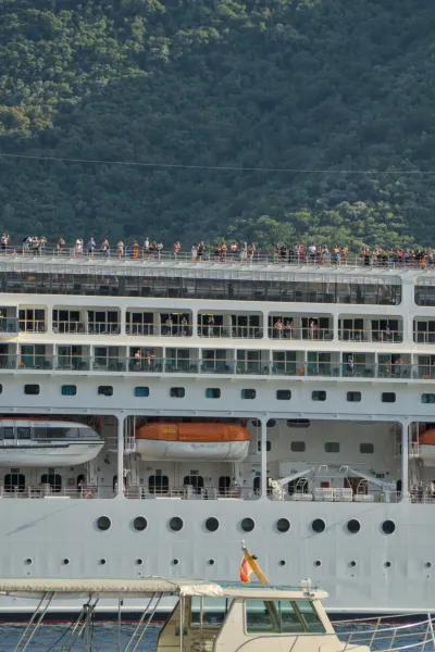 Pasajeros en la cubierta superior de un crucero se despiden de Kotor con un fondo de montaña verde.