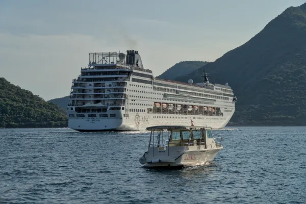 Una nave da crociera lascia la Baia di Kotor, Montenegro, con una barca più piccola in primo piano.