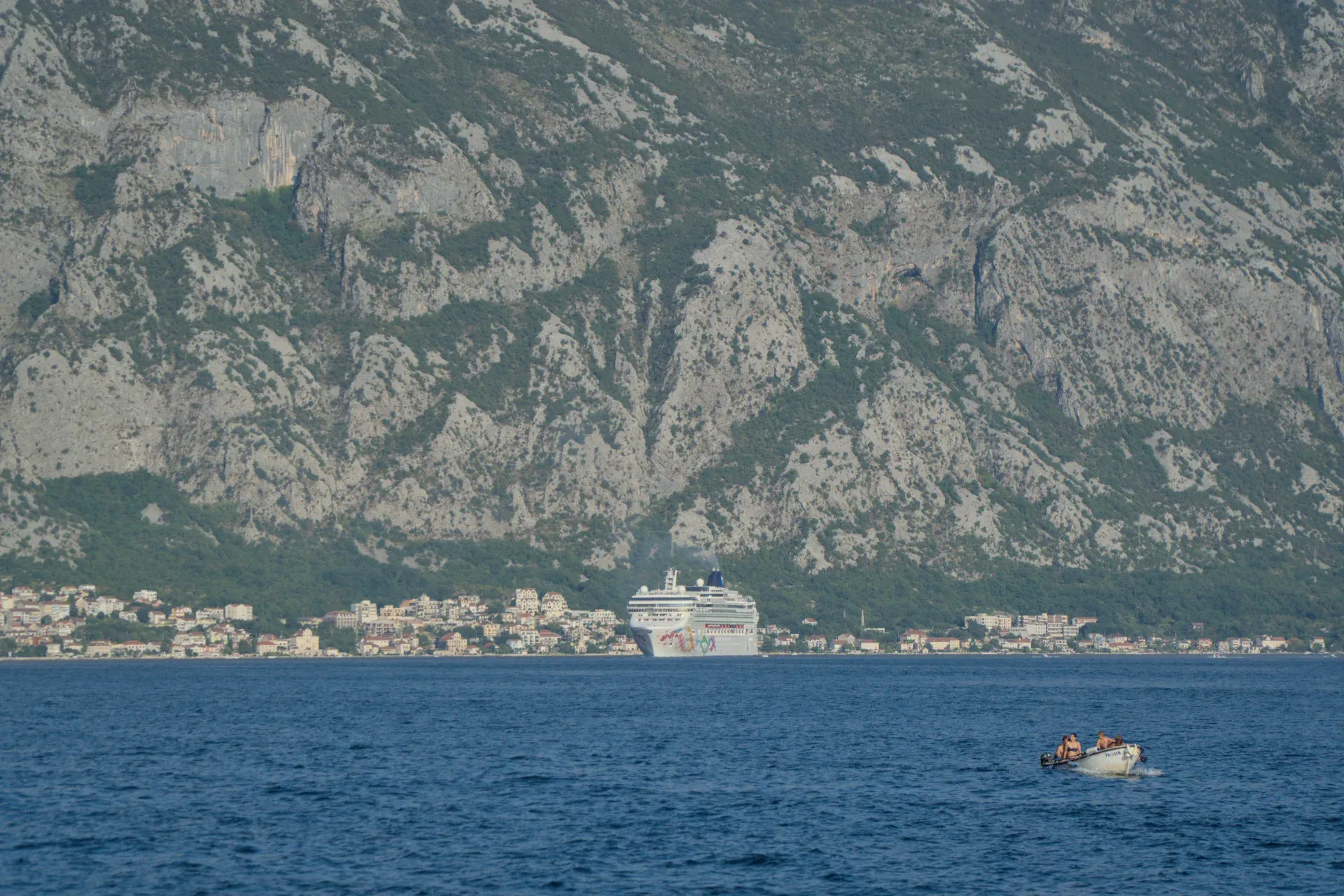 Un paquebot et de petits bateaux sur la mer devant la ville de Kotor avec ses maisons et les montagnes derrière.
