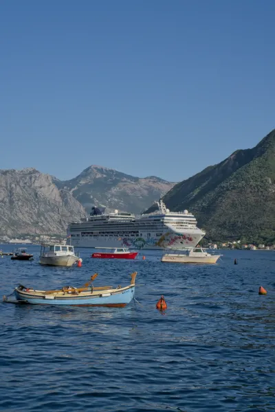 Ein großes Kreuzfahrtschiff verlässt die Bucht von Kotor durch Perast, mit kleineren Booten im Vordergrund.