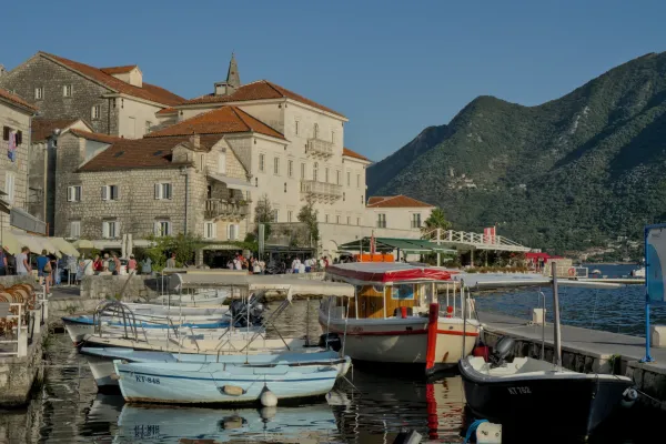 Perast, Crna Gora, uhvaćen u zlatnom satu, sa brodovima u luci i planinama u pozadini.