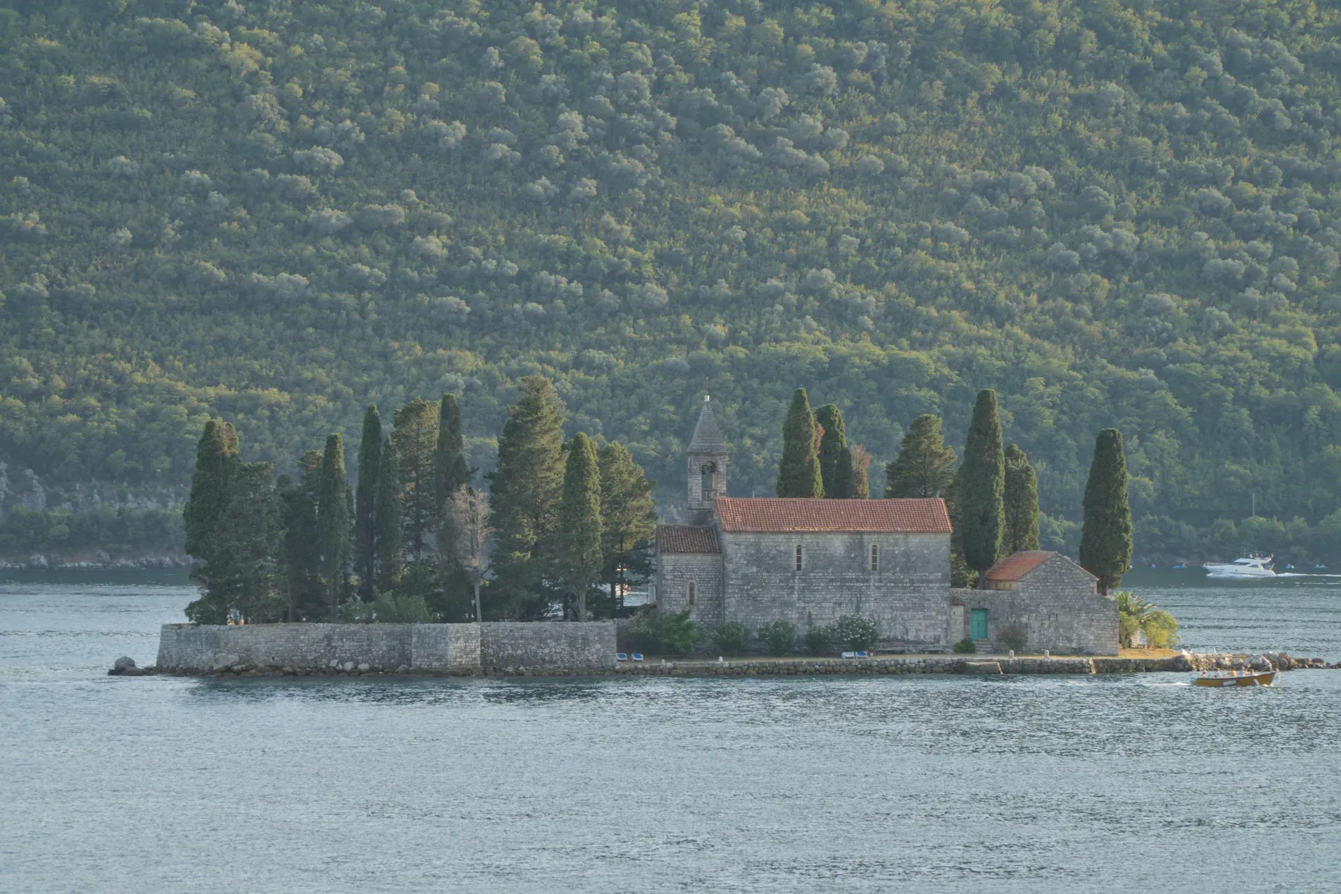 Il Monastero di San Giorgio a Perast, Montenegro, su un'isola con cipressi e acqua calma, contro una collina boscosa.