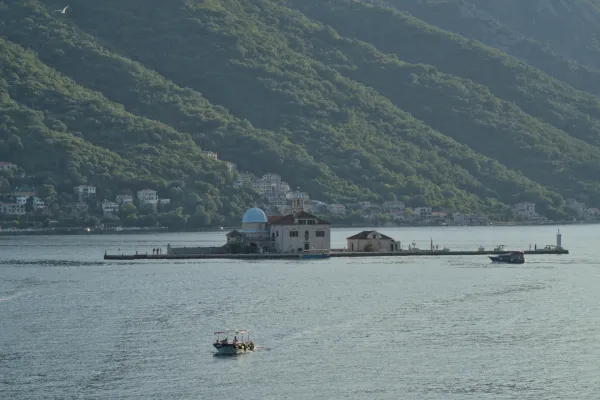 La iglesia insular Gospa od Škrpelja en Kotor, Montenegro, al atardecer, con colinas verdes de fondo.