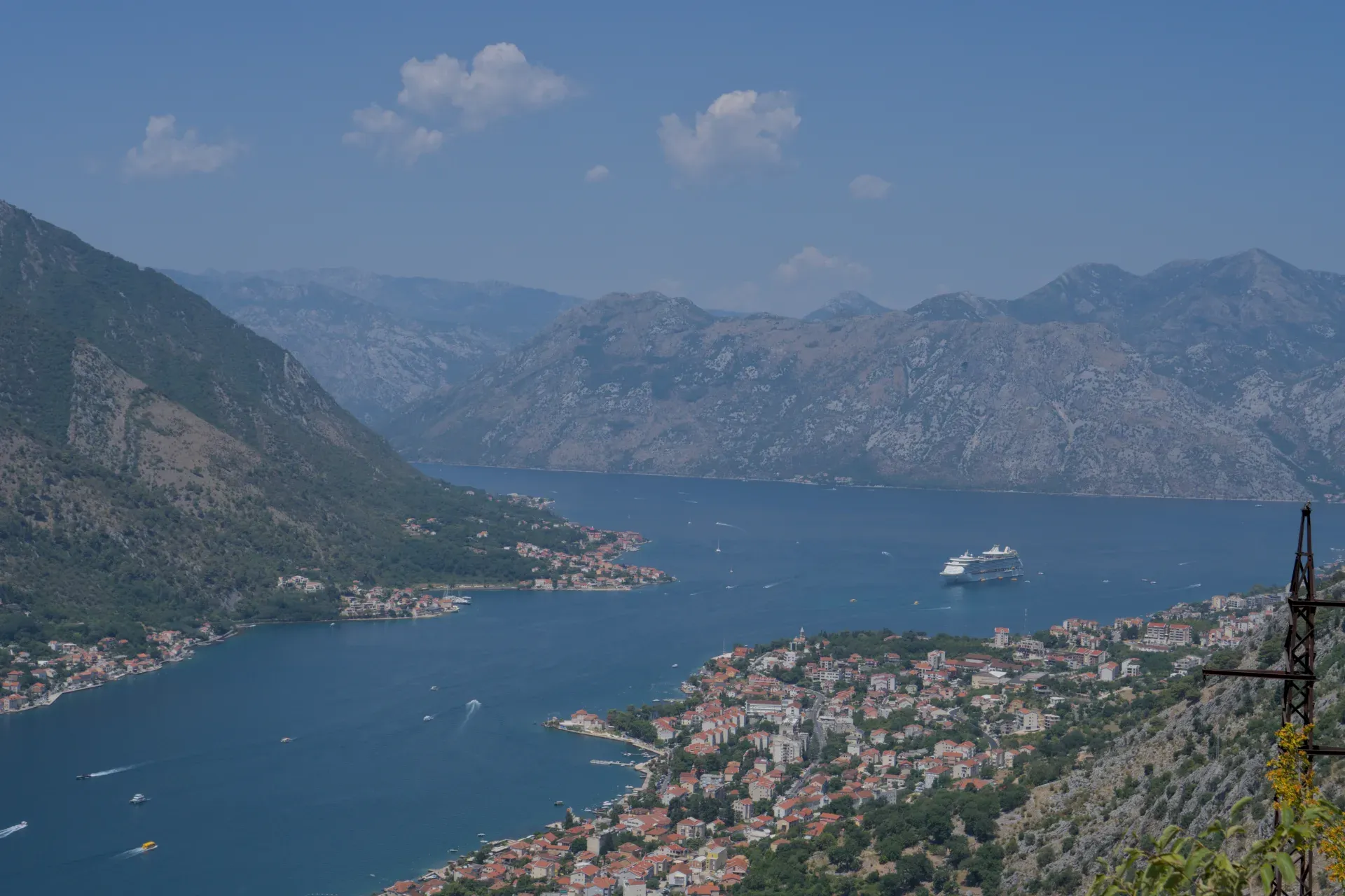 Ein großer Kreuzliner fährt langsam in die malerische Bucht von Kotor ein, umgeben von Bergen und einer Küstenstadt.
