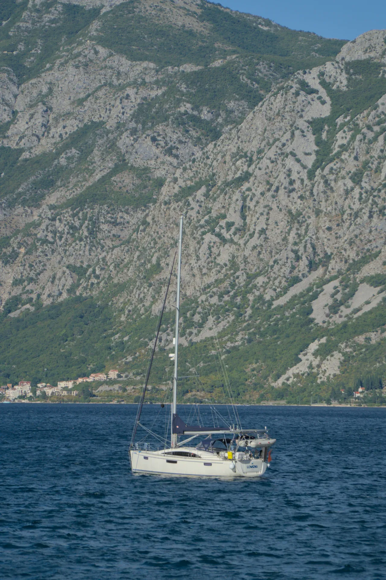 Eine weiße Yacht segelt in der Bucht von Kotor vor einer Bergkulisse, ein Kunstwerk für maritime Interieurs.