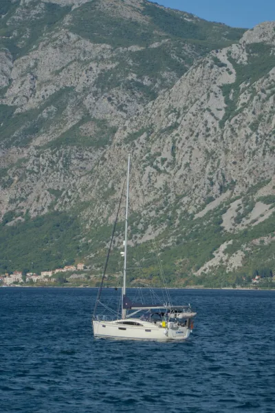 Uno yacht bianco che naviga nella Baia di Kotor su uno sfondo montuoso, arte per interni costieri.