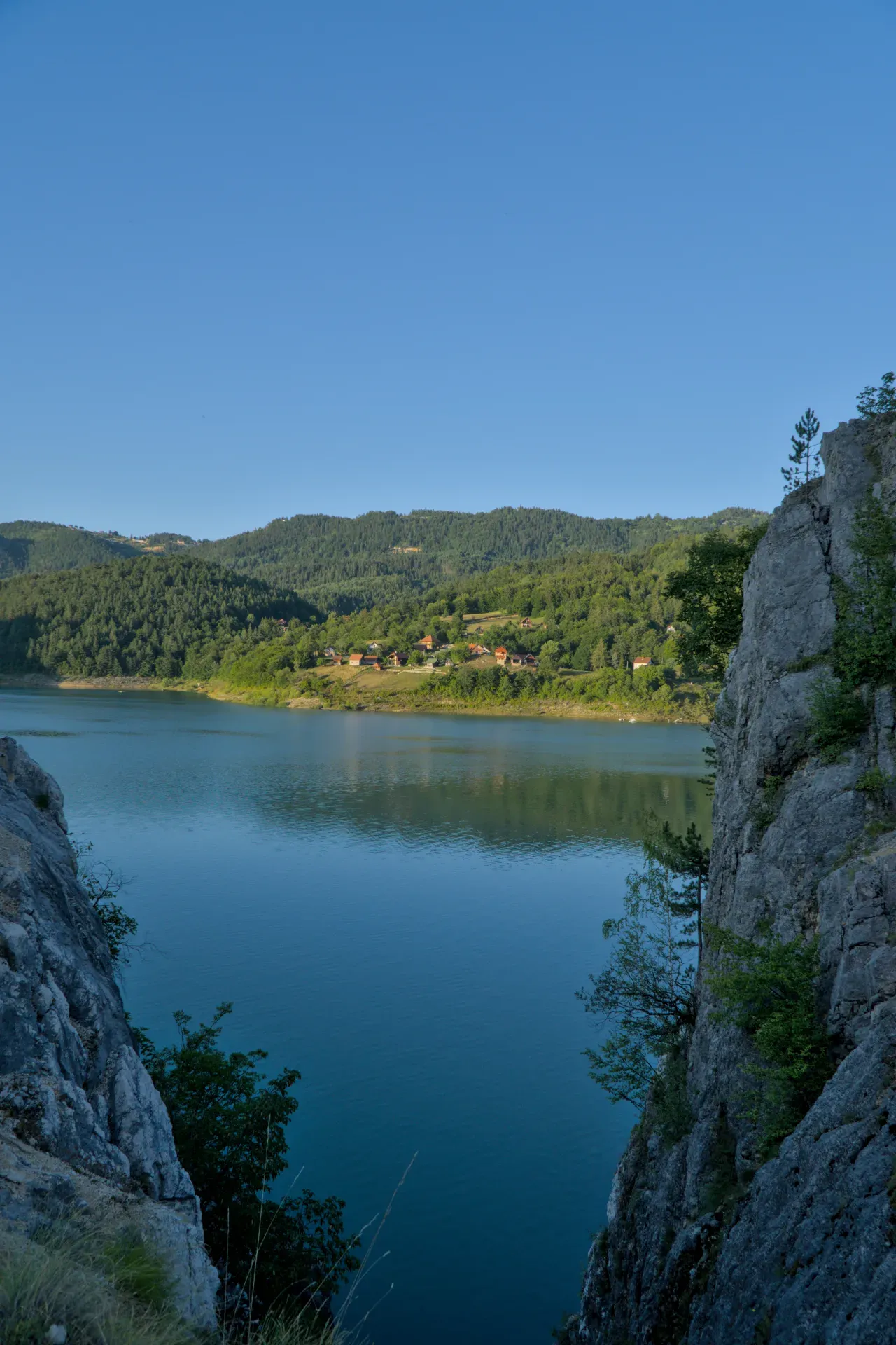 Coucher de soleil au lac de Zaovine, Serbie, avec des collines boisées et un premier plan rocheux.