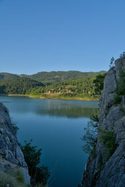 Coucher de soleil au lac de Zaovine, Serbie, avec des collines boisées et un premier plan rocheux.
