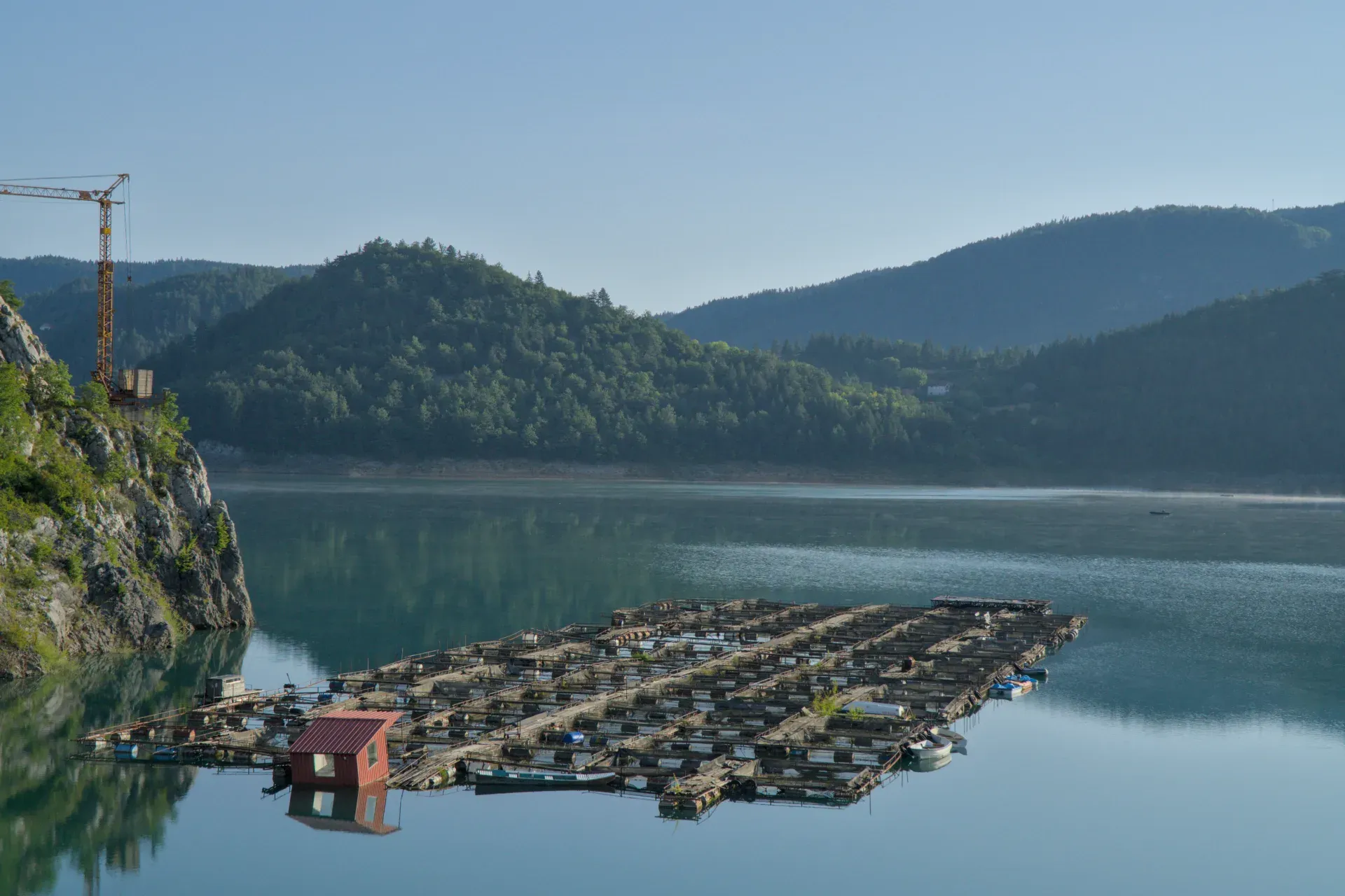Friedliche Morgendämmerung am See Zaovine mit Nebelschwaden und Spiegelungen der Berge.