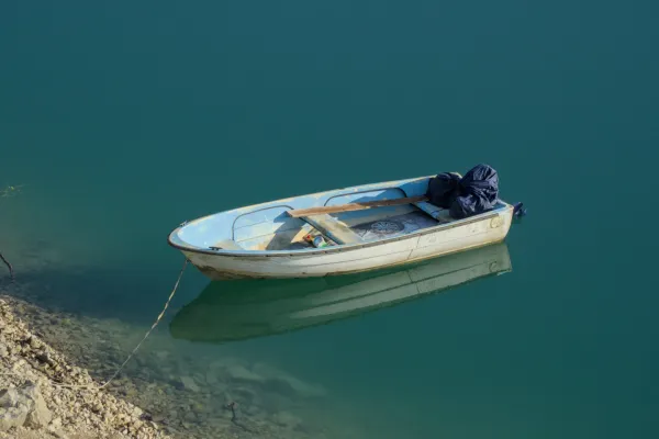 Ein weißes Boot mit blauen Akzenten liegt vertäut auf dem ruhigen, türkisfarbenen Wasser des Zaozisko Sees bei Sonnenaufgang.