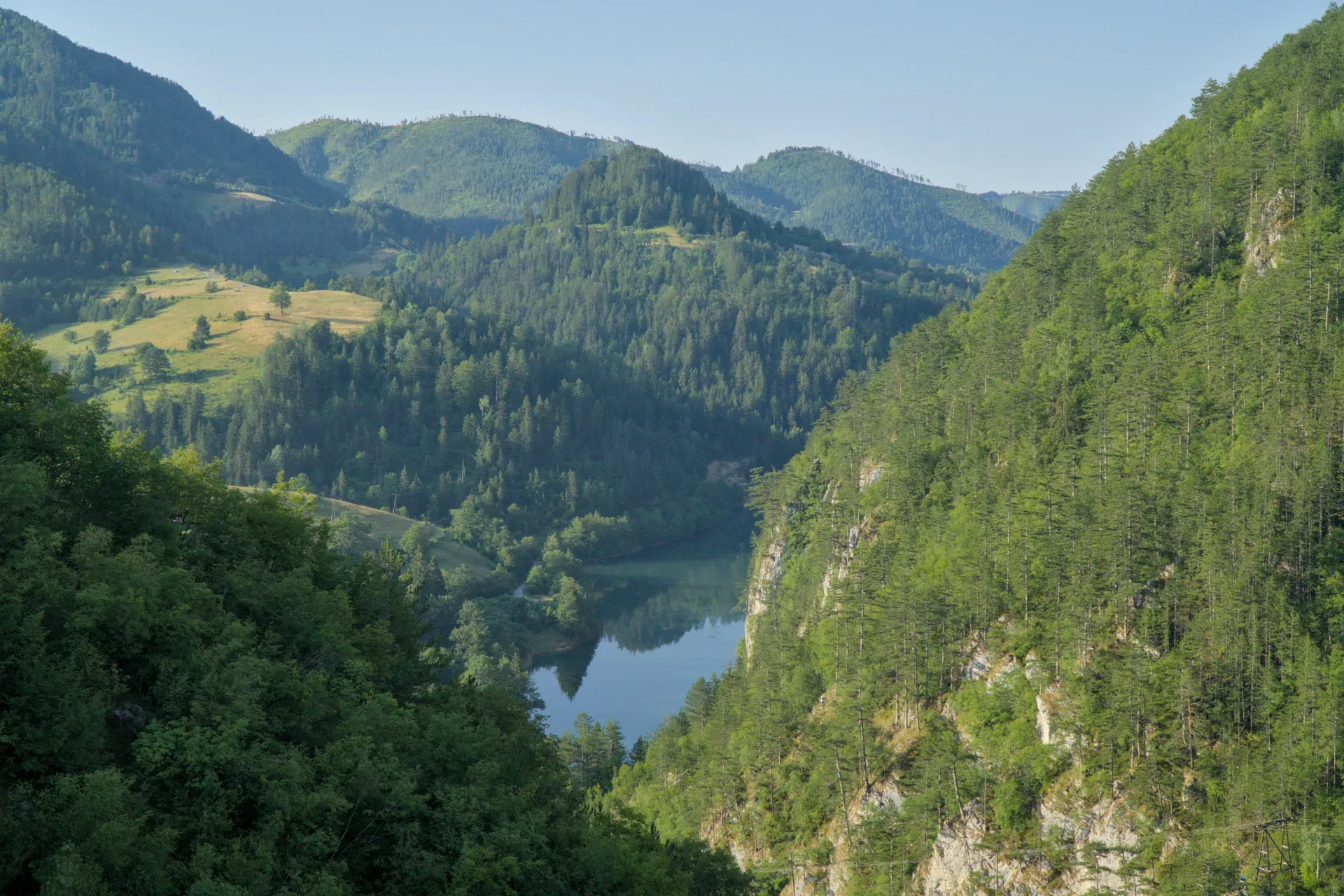 Vista panoramica dalla diga Laziĉa verso il lago Spajiĉ, incorniciata da lussureggianti foreste montane e prati.