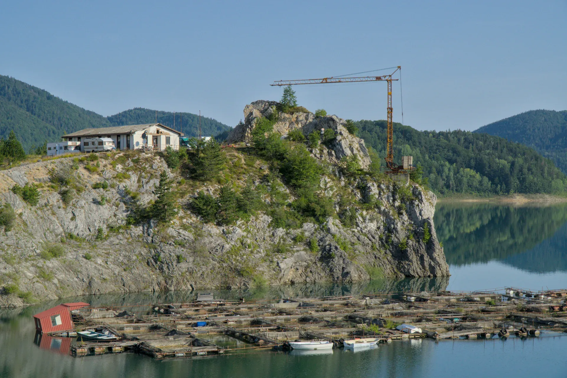 Buntes Morgenlicht erhellt den Zaovine See in Serbien, mit Bergen und Fischfarmen im Vordergrund.