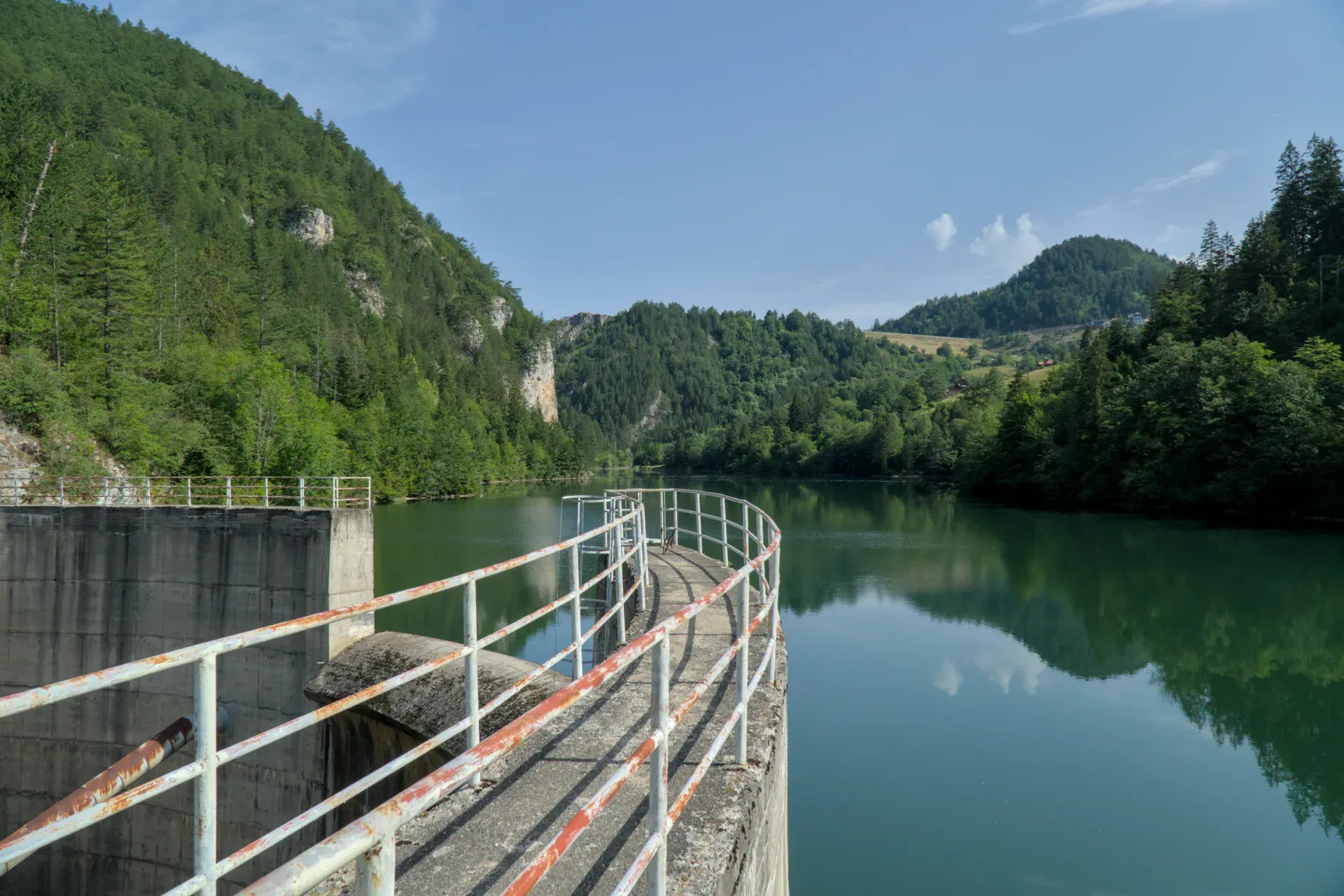 Le barrage du lac Spajići en Serbie, avec sa passerelle incurvée et le paysage montagneux verdoyant environnant.