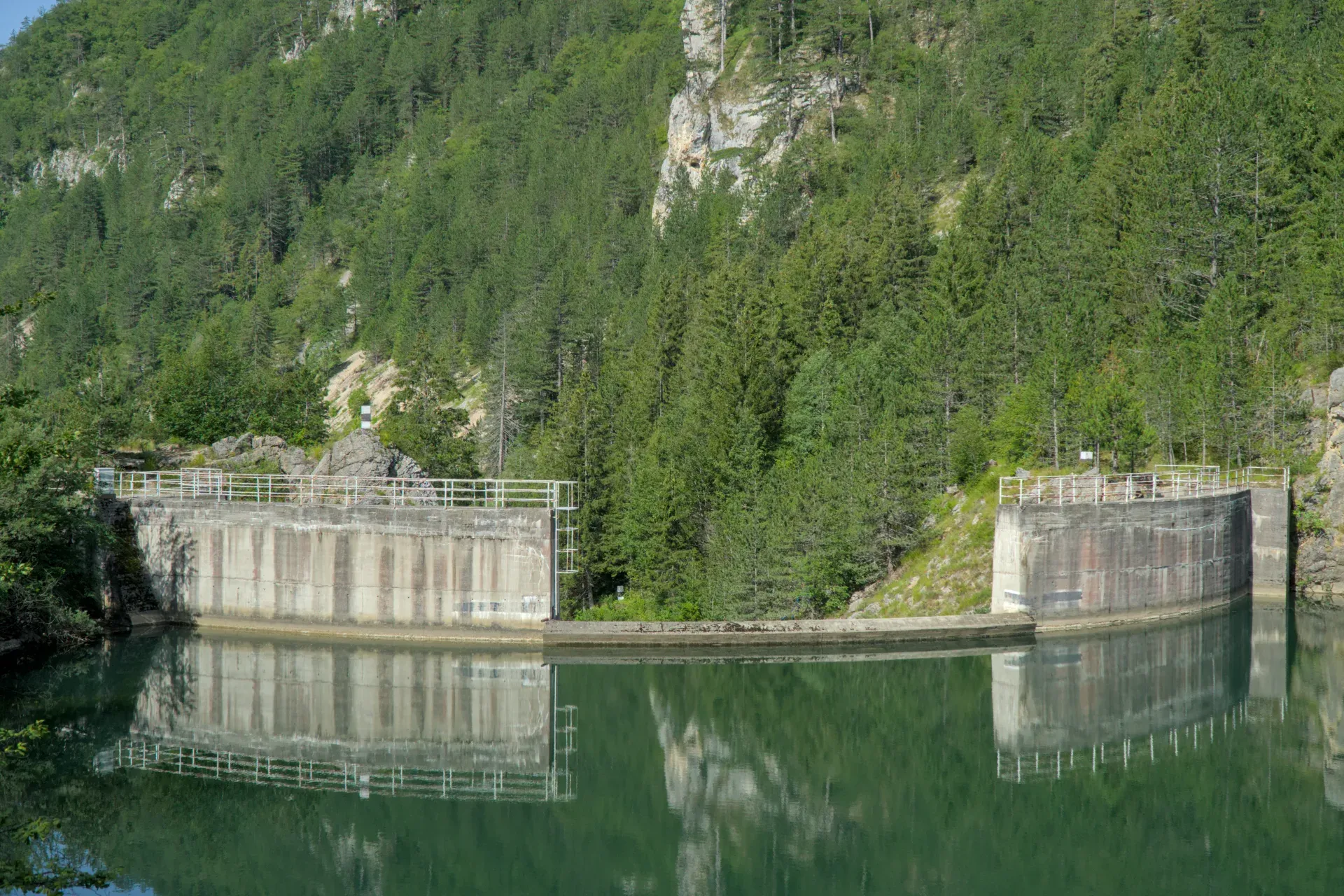 La diga del Lago Spajići a Zaovine, Serbia, che si riflette nell'acqua calma, circondata da montagne e foreste verdi.