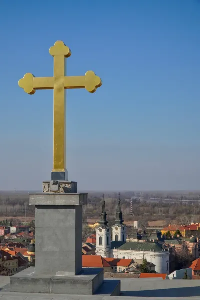 Une croix dorée proéminente se dresse sur un ciel bleu clair, surplombant une vue panoramique de Sremski Karlovci, Serbie.