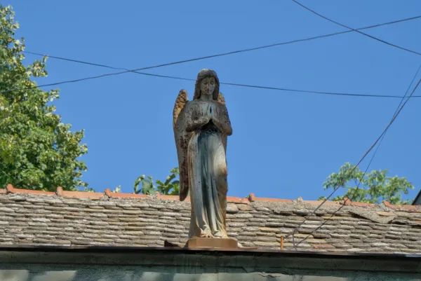 Skulptura anđela na krovu kuće u Novom Sadu, Srbija, na pozadini plavog neba.