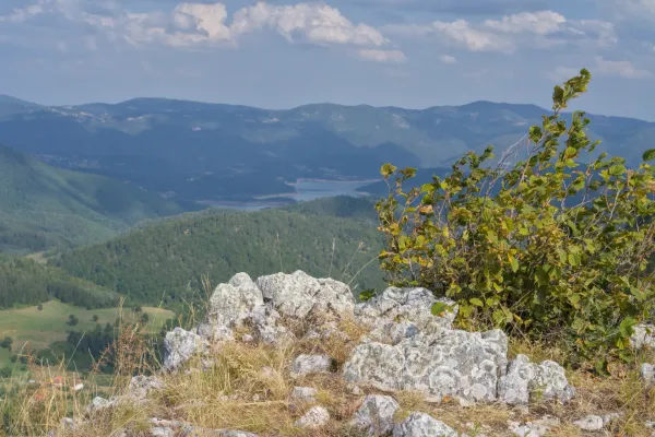 Lac Zaovine vu des montagnes Jankovica, Serbie, avec des rochers et de la végétation au premier plan et des collines ondulantes.