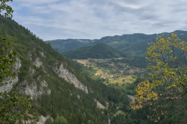 Panoramablick von Ravna Stena auf das Dorf Spaichi im Tara Nationalpark, Serbien, mit bewaldeten Hügeln und Fluss.