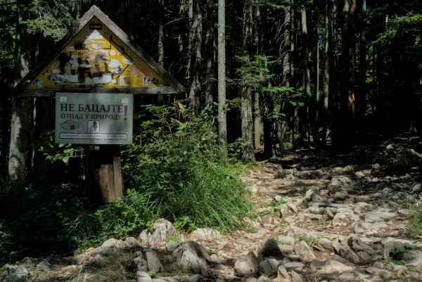 Un sentiero roccioso nella foresta conduce al punto panoramico di Banjska Stena in Serbia, con un cartello che invita alla conservazione della natura.