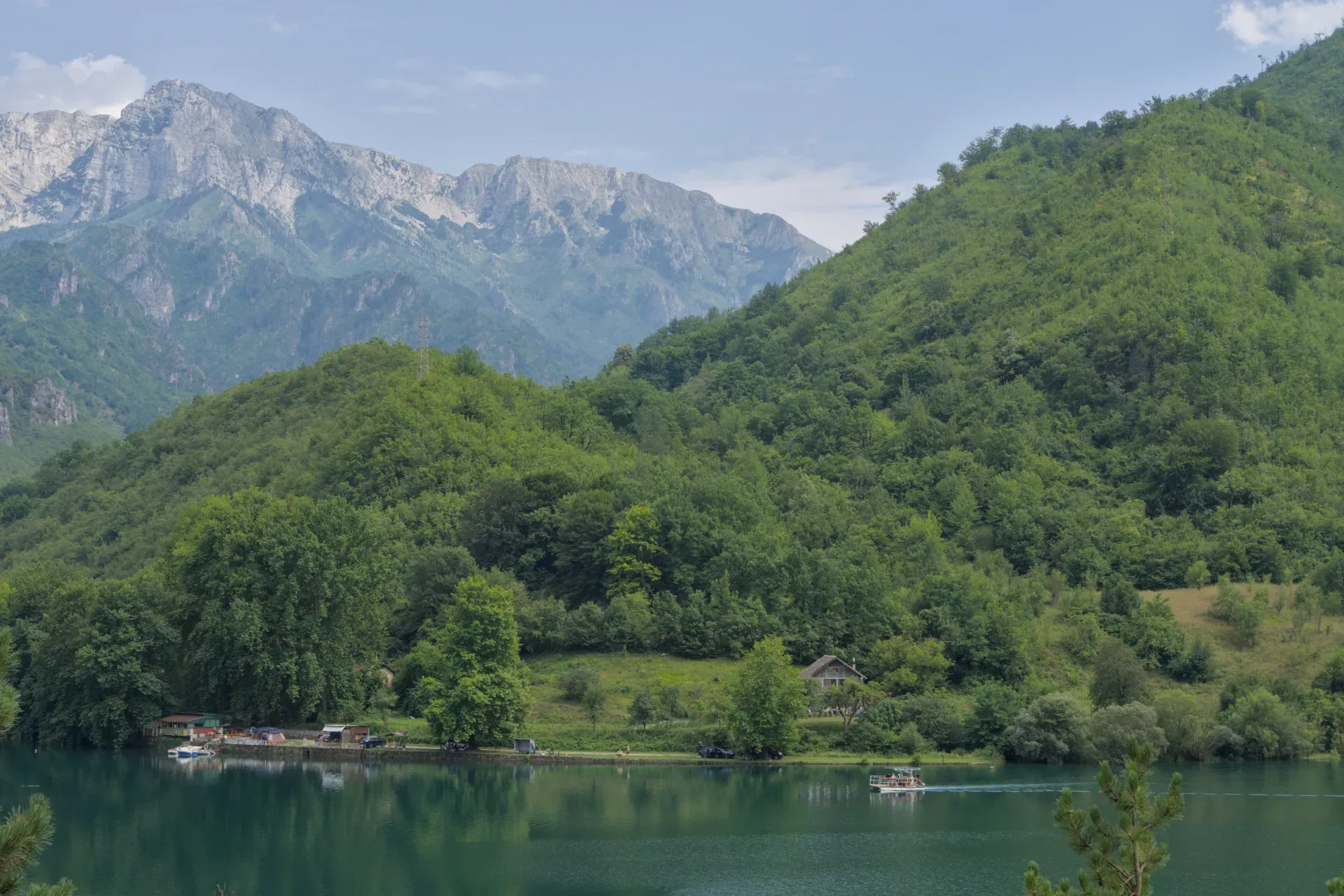 Malerischer Weg von Sarajevo nach Mostar: Ein Bergsee mit Boot und grünen Hügeln unter bewölktem Himmel.