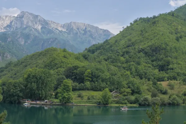 Route pittoresque de Sarajevo à Mostar : un lac de montagne avec un bateau et des collines vertes sous un ciel nuageux.