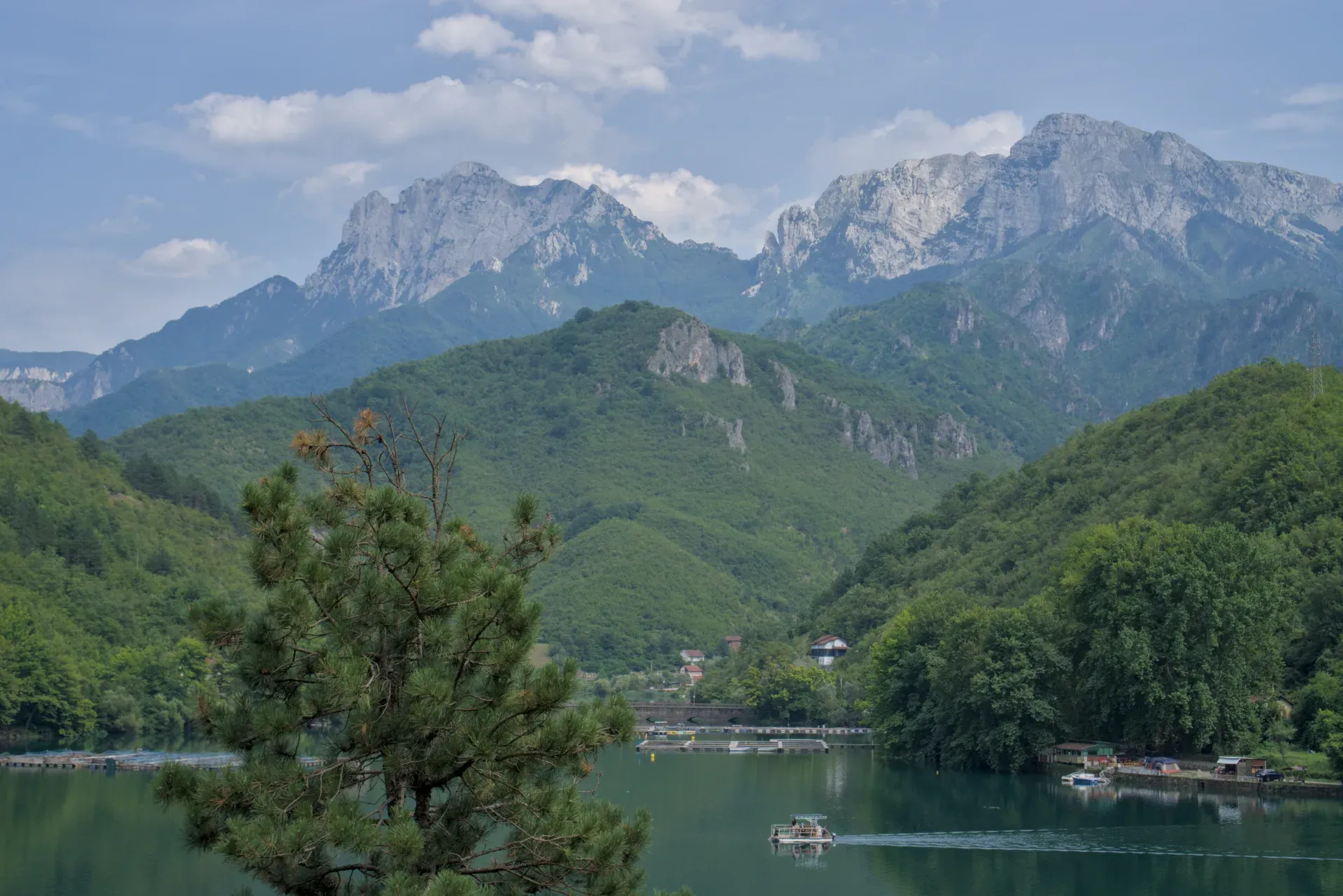 Una barca viaggia su un bellissimo lago, sullo sfondo di montagne verdi, in direzione di Mostar.