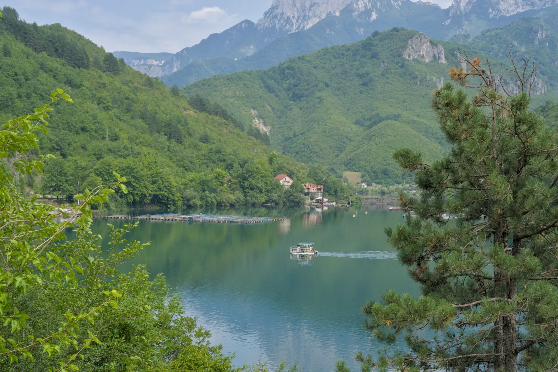 Un bateau navigue sur un lac azur avec des montagnes vertes et une maison au bord, idéal pour l'art mural.